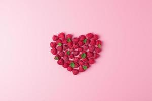 Creative summer concept. Heart shape made from fresh berries snd mint leaves on pink background. Flat lay, copy space. photo