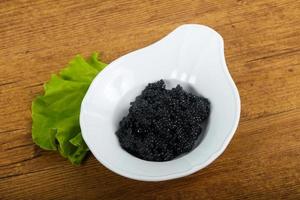 caviar negro en un recipiente sobre fondo de madera foto