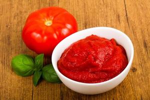 Tomato paste in a bowl on wooden background photo