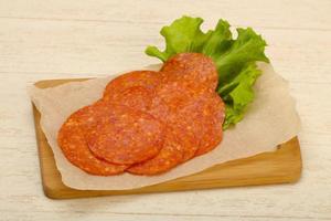 Pepperoni sausage on wooden board and wooden background photo