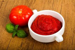 Tomato paste in a bowl on wooden background photo