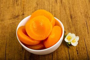 Canned peaches in a bowl on wooden background photo