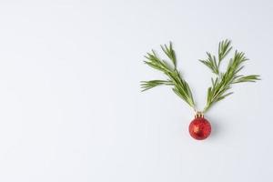 fondo mínimo blanco navideño con cuernos de reno hechos con bola roja y romero. endecha plana, espacio de copia foto
