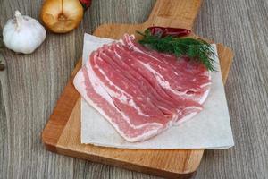 Raw bacon on wooden board and wooden background photo