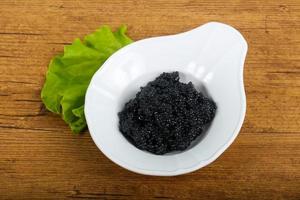 Black caviar in a bowl on wooden background photo