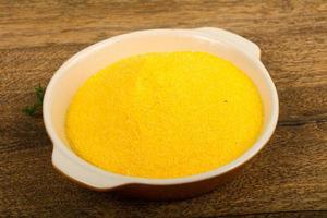 Raw polenta in a bowl on wooden background photo