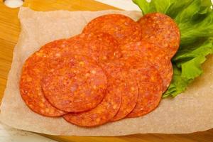 Pepperoni sausage on wooden board and wooden background photo