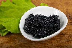 caviar negro en un recipiente sobre fondo de madera foto