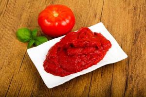 Tomato paste in a bowl on wooden background photo