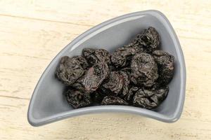 Dried plums in a bowl on wooden background photo