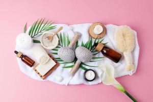 Spa treatment with natural skin care products, candles and herbal bag, towel on pink background. Flat lay. photo