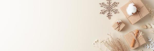 adornos navideños con regalos de embalaje en papel artesanal y flores sobre fondo beige. concepto de vacaciones de navidad sin desperdicio. endecha plana, espacio de copia foto