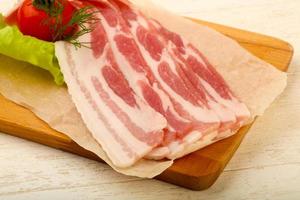 Raw bacon on wooden board and wooden background photo