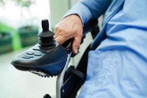 Asian elderly woman disability patient sitting on electric wheelchair in park, medical concept. photo