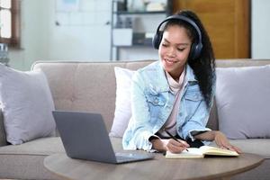 Smiling Asian young female using headphones looking at laptop screen listen and learning online courses. photo