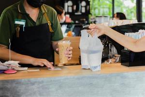 Barista wearing face mask serving coffee in plastic bag to take out in cafe. photo