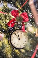 reloj de navidad lazo rojo en la rama de un árbol foto