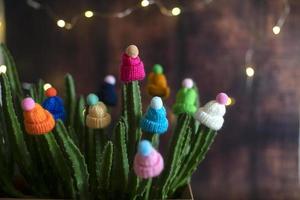 Multicolored woolen decorative hats with pompoms are worn on the stems of a live cactus in a pot at home. Funny and creative. Winter concept. photo