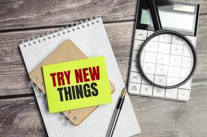 TRY NEW THINGS words on green sticker and calculator, magnifying glass on wooden background photo