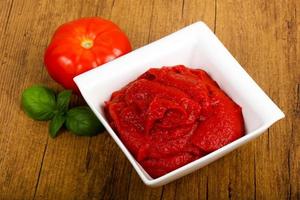 Tomato paste in a bowl on wooden background photo