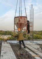 The workers on a building infrastructure roof with machinery and tools. Pouring concrete into a mold photo