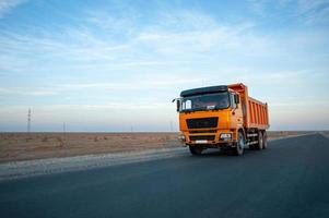 un camión volquete naranja en una carretera del desierto contra un hermoso fondo del cielo foto