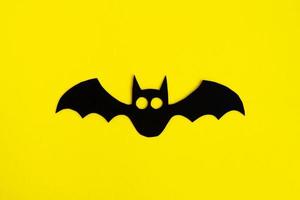 Holiday decorations for Halloween. Black paper bat on a yellow background, top view. photo