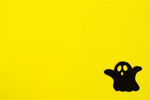 Holiday decorations for Halloween. Black paper ghost on a yellow background, top view. photo