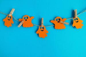 Holiday decorations for Halloween. Orange paper ghosts hanging on a rope on a blue background with copy space. photo