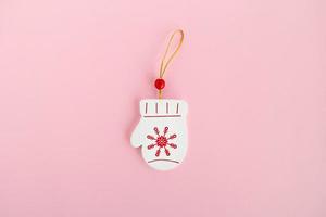 Wooden Christmas and New Year decoration in the form of mitten with painted red snowflake on a pink background, top view. photo