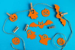 Preparation for Halloween. Orange paper decorations - ghosts, pumpkins and bats on a rope with pins on a blue background, top view. photo