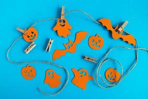 Preparation for holiday. Decorations for Halloween - orange paper ghosts, pumpkins and bats on a rope with pins on a blue background. photo