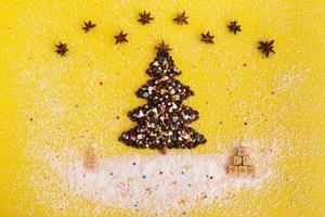 árbol de navidad hecho de granos de café y regalos de navidad hechos de gofres decorados con chips de coco, estrella de anís y rociado culinario multicolor sobre un fondo amarillo, vista superior. foto