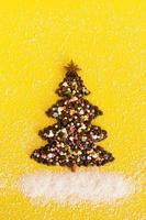 Christmas tree made from coffee beans and decorated anise star, multicolored culinary sprinkling and coconut chips on a yellow background, top view. photo