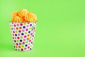Small colorful bucket filled with yellow meringue on a green background. Minimal concept with copy space. photo