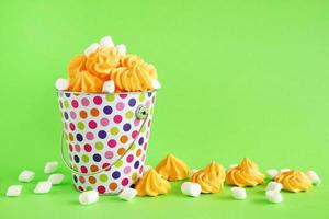 Small colorful bucket filled with yellow meringue and white marshmallows on a green background. Minimal concept with copy space. photo