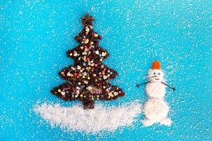 Christmas tree and snowman made from coffee beans and coconut chips decorated anise star, multicolored culinary sprinkling on a blue background, top view. photo