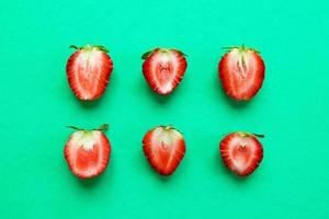 Two rows from halves of red ripe strawberry on a bright turquoise background, top view. Healthy summer food. photo