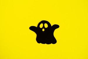 Holiday decorations for Halloween. Black paper ghost on a yellow background, top view. photo