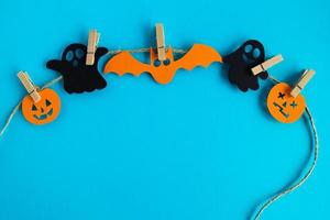 Holiday decorations for Halloween. Black paper ghosts and orange paper pumpkins and bat hanging on a rope on a blue background with copy space. photo