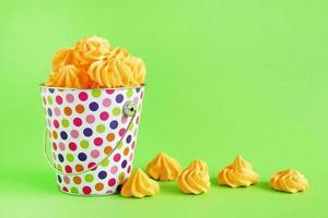 Small colorful bucket filled with yellow meringue on a green background. Minimal concept with copy space. photo