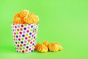 Small colorful bucket filled with yellow meringue on a green background. Minimal concept with copy space. photo