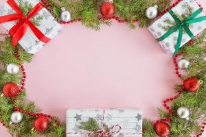 Top view on a frame from red and silver Christmas decorations, gift boxes and fir branches on a pink background with copy space. photo