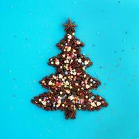 Christmas tree made from coffee beans and decorated anise star and multicolored culinary sprinkling on a blue background, top view. photo