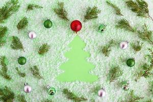 composición invernal con ramas de abeto decoradas con árboles de navidad, adornos navideños rojos, verdes y plateados sobre un fondo verde con nieve artificial, puesta plana. tarjeta de felicitación para año nuevo. foto
