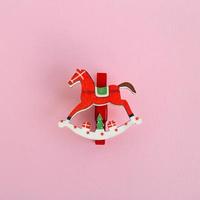 Red wooden Christmas and New Year decoration in the form of horse on a pink background, top view. photo