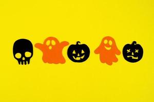 Holiday decorations for Halloween. Orange paper ghosts and black paper pumpkins and skull on a yellow background, top view. photo