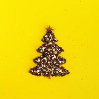 Winter composition with Christmas tree made by coffee beans and decorated anise star, cinnamon stick and multicolored culinary sprinkling on a yellow background, flat lay. Greeting card for New Year. photo