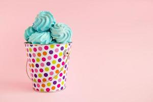 Small colorful bucket filled with blue meringue on a pink pastel background. Minimal concept with copy space. photo