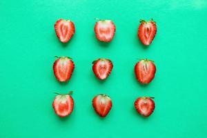 Three rows from halves of red ripe strawberry on a bright turquoise background, top view. Healthy summer food. photo